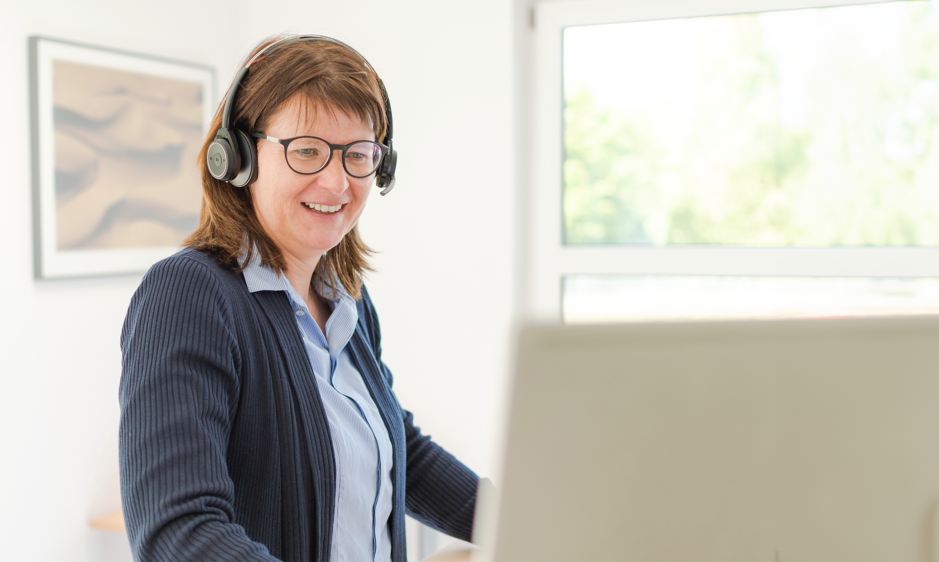 Mitarbeiterin im Kundenservice arbeitet am Computer mit Headset als Beispiel für E-Commerce- und Omnichannel-Lösungen von Dynamity